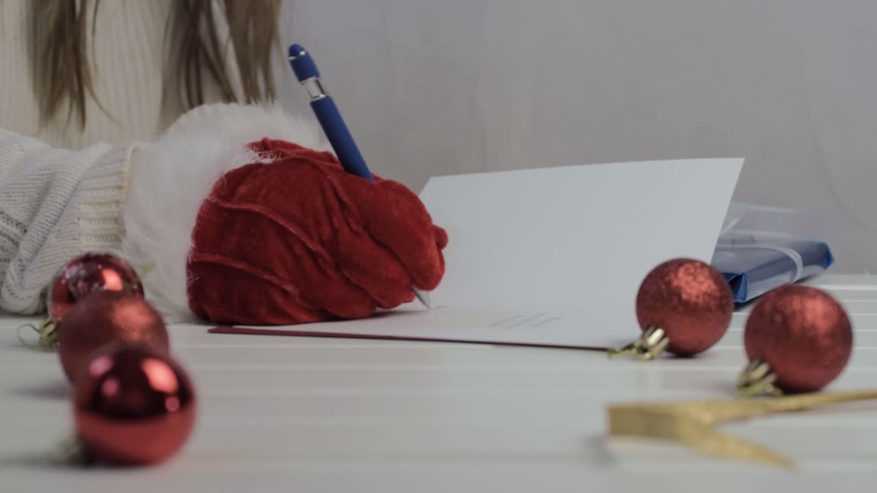 Woman writing out Christmas greeting cards wearing red Santa gloves wide shot