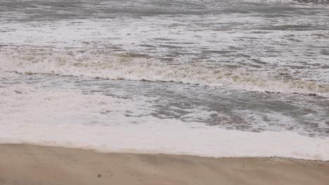 역동적인 바다 파도가 구름이 가득한 하늘 아래 모래 해변에 부히며 움직이는 자연의 힘을 포착합니다.