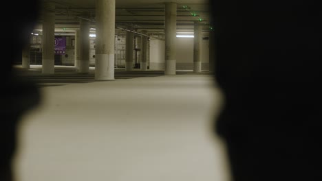 Feet-of-male-walking-in-front-of-screen-and-into-empty-underground-parking-lot-in-Metzingen,-Germany,-Baden-Wurttemberg,-Europe,-panning-view-angle