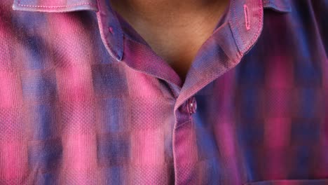 closeup of a man buttoning his pink plaid shirt