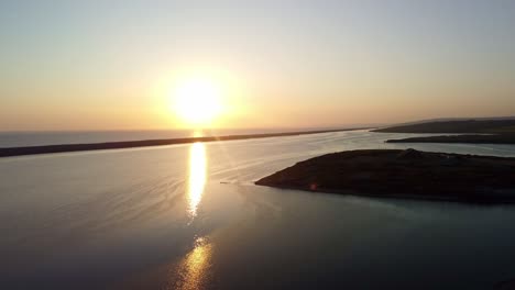 The sun setting over the coast of Weymouth East Fleet, Dorset. Aerial footage captures this tranquil scene with the sun reflecting across the sea and the camera moves to the right.
