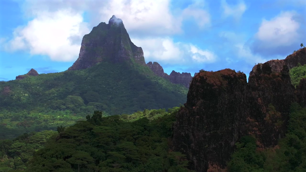 Moorea, Franska Polynesien: Dramatiska vulkaniska höga, taggiga toppar, oländig terräng. Mount Rotui, Mt Toheia. Flygdrönarvy över Belvedere utsiktsplats, CooksOpunohu Bay. Solig morgon, blå himmel, moln, drönare cirklar höger
