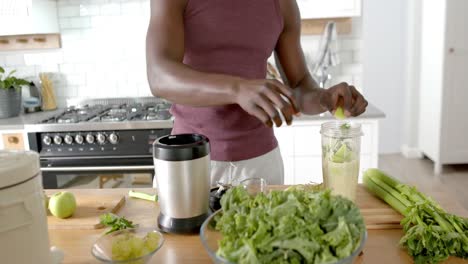 Sección-Media-De-Un-Hombre-Afroamericano-Preparando-Batidos-Saludables-En-La-Cocina-De-Casa,-Cámara-Lenta