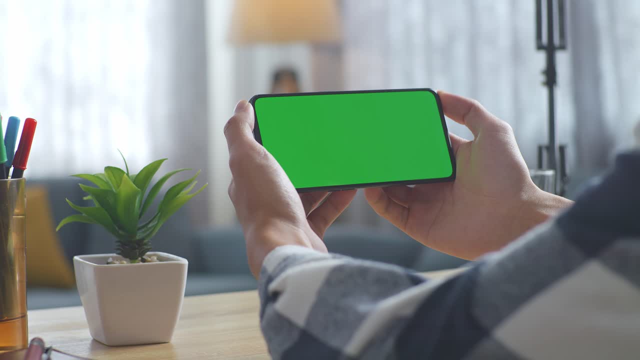 초록색 화면을 모방한 노트북 컴퓨터의 상단에서 아래로 볼 때, 펜, 안경, 그리고 물 한 잔을 가진 노트북 에 나무 사무실 책상 위에 크로마키 디스플레이가 있습니다.