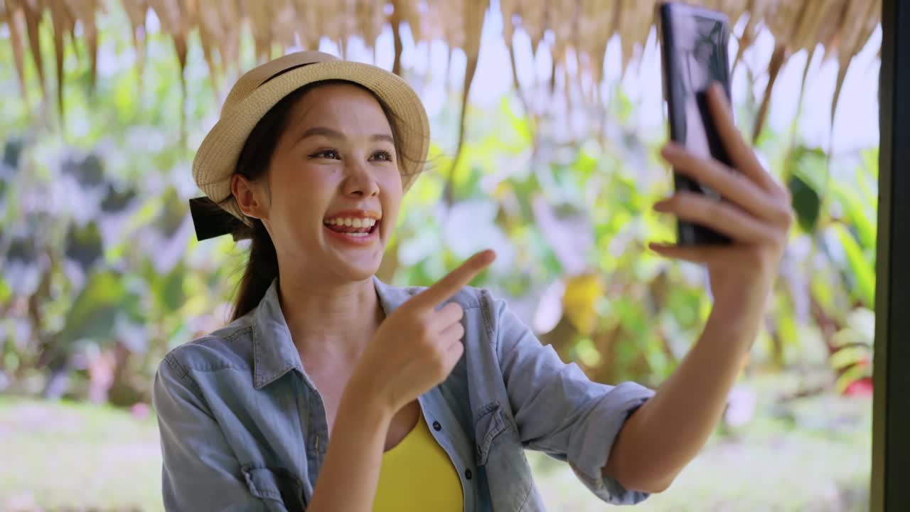 say hi gesture greeting video calling to family abroad connection,asian female digital nomad using smartphone calling to say hi her family or friend while vacation travel at the beach working anywhere