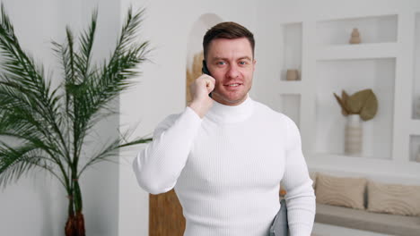 Attractive Caucasian male in white shirt holding a phone at his ear. Cropped image of a businessman calling to partners and smiling.