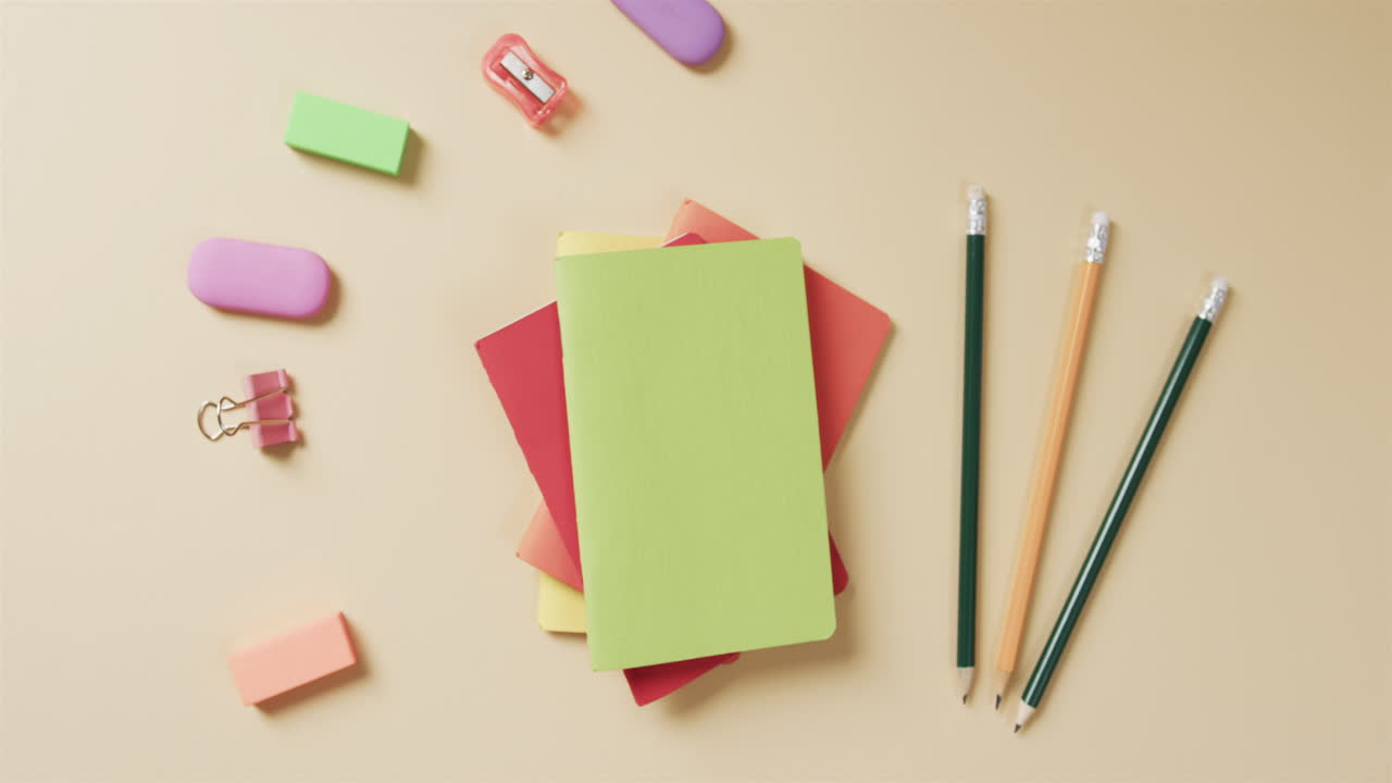 Overhead view of colourful notebooks with school stationery on beige background, in slow motion