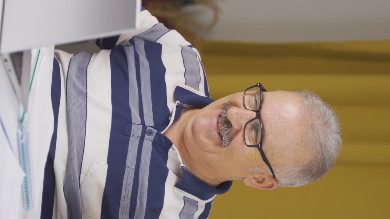 video vertical de un anciano trabajador de oficina en casa se regocija con lo que ve en la computadora portátil.