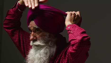 close up low key studio lighting shot of senior sikh man with beard tying fabric for turban against dark background 4