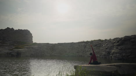 woman practicing yoga by tranquil quarry lake in the morning sun with soft reflections on water, slow motion