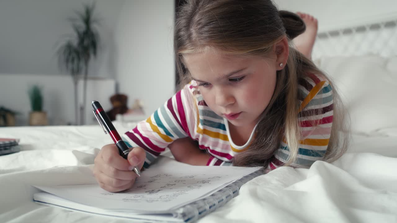 Elementary age girl studying while lying on front on the bed