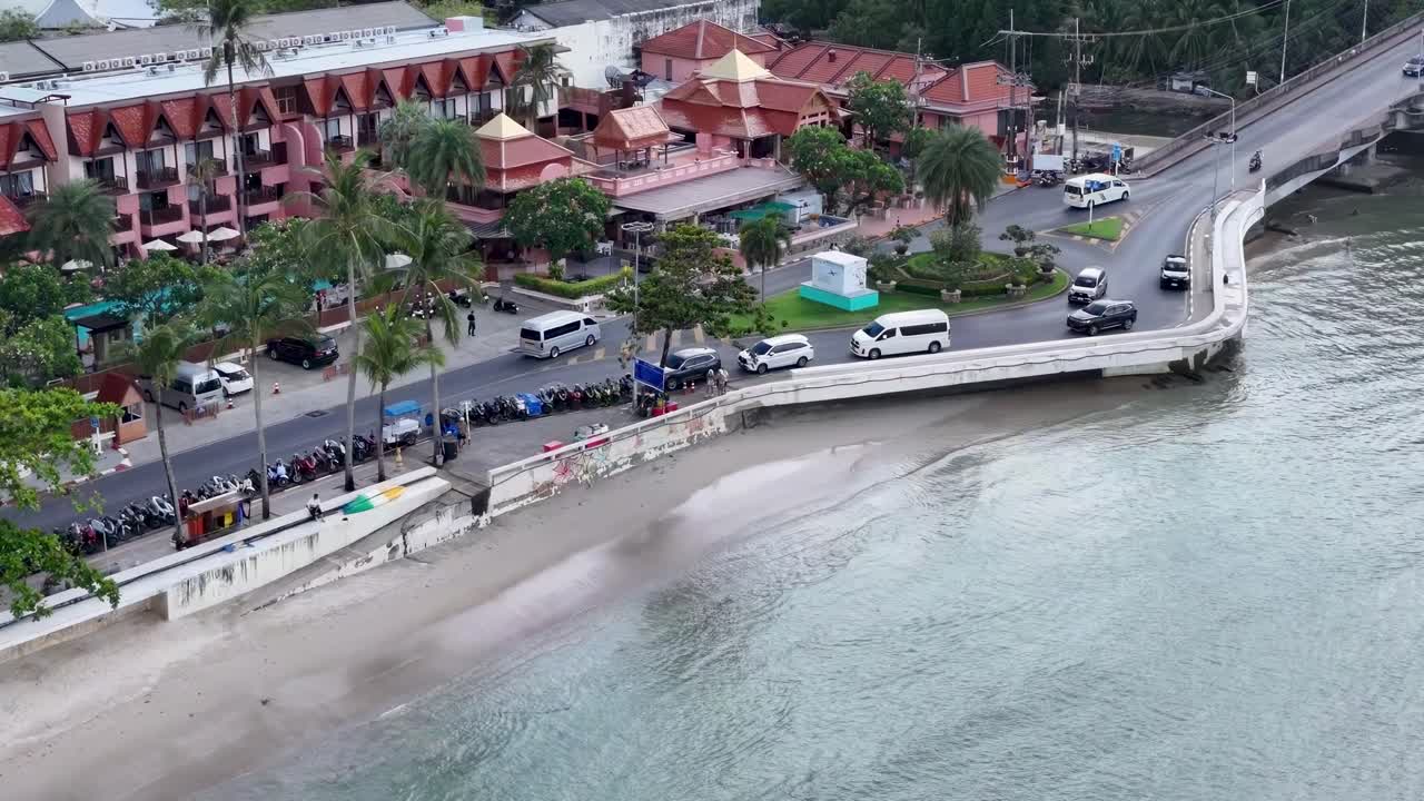 Aerial view of a coastal road beside a vibrant resort in Phuket, Thailand.