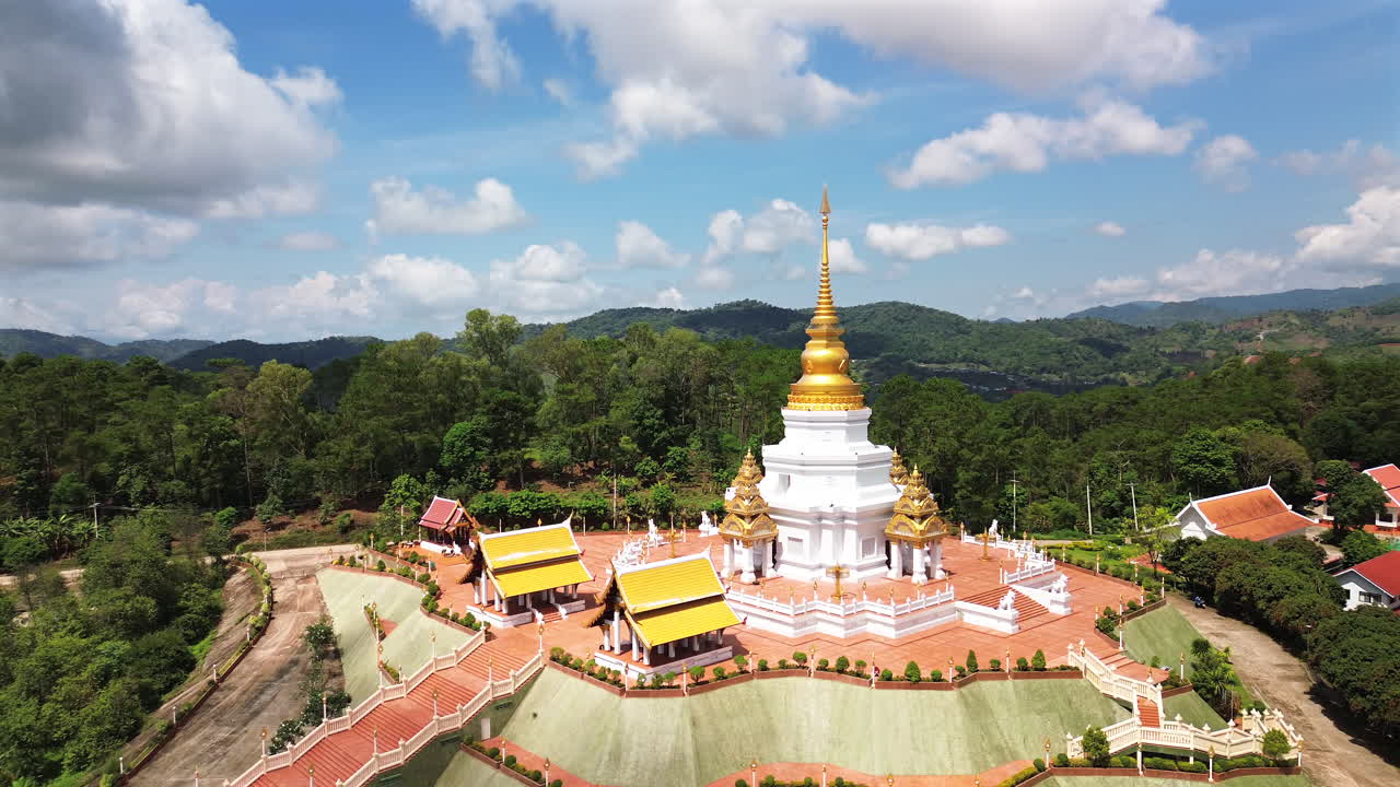 Aerial establishing orbit of Wat Phra That Santitham, Mae Salong, Chiang Rai Thailand, vivid golden stupa in sunlight at hill temple, peaceful sky and trees in background