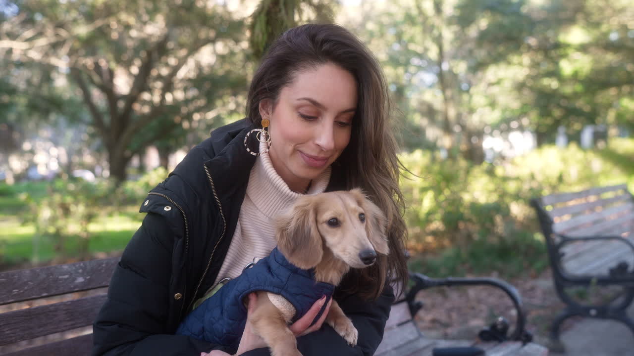 Woman pet owner kisses her dachshund weiner dog on a park bench in autumn