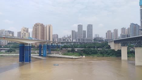 landscape clip of train rails over a river with a train passing with the city of chongqing , china in the background