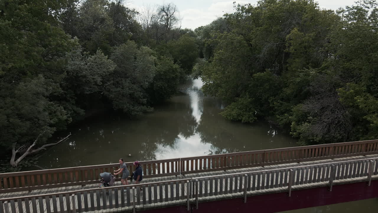 encantadora pareja con un niño pequeño paseando por un puente de madera sobre el río sucio en st-eustache, quebec, canadá - disparo de drones