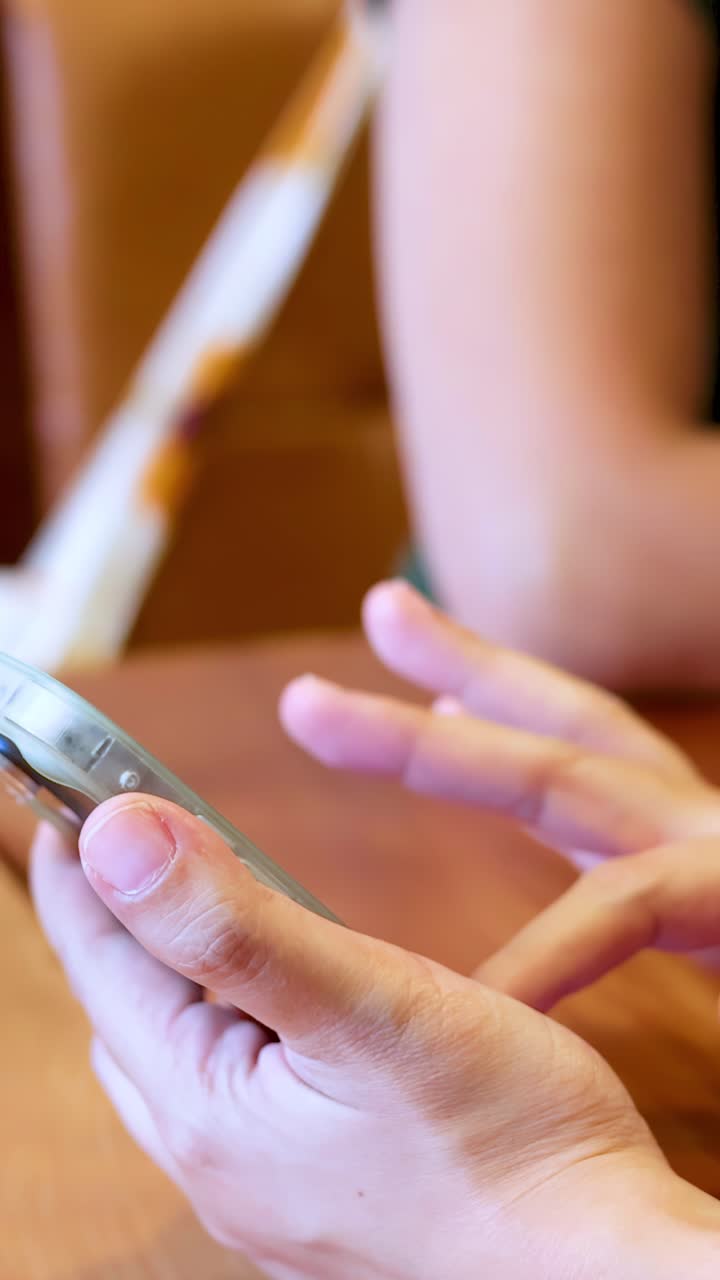 Primo piano di mani che scorrono e toccano lo schermo di uno smartphone su un tavolo di legno.