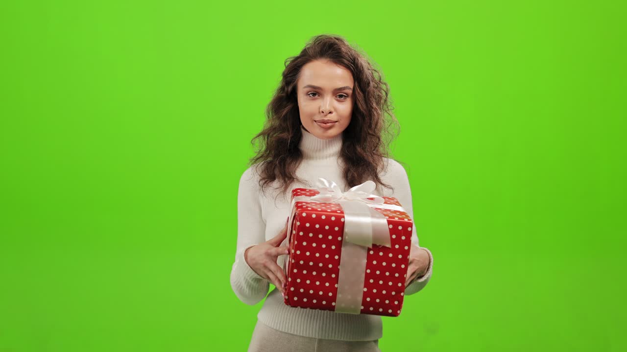 그 여자는 서서 카메라를 바라보고 있습니다. 그녀는 당신에게 선물을 주고 있습니다. 그녀는 녹색 배경에 서 있습니다. 녹색 화면.