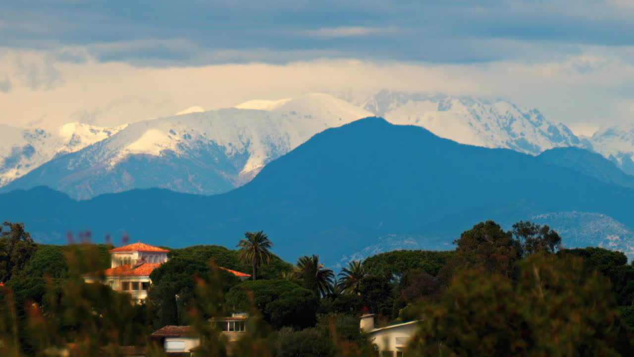 Distant view of orange villas surrounded by green trees with the mountains on the background on a cloudy day