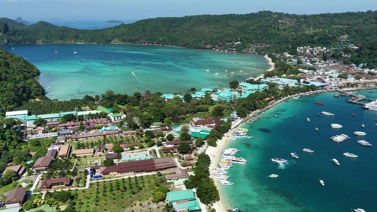 Spiaggia e porto di Phi Phi Don con mare turchese e barche, drone che stabilisce lo sfondo dalla collina lungo la costa sinuosa