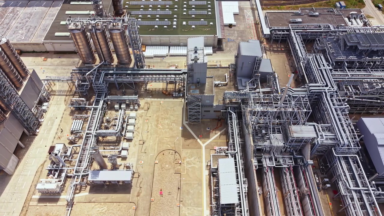 Vista di un grande impianto industriale con serbatoi di stoccaggio e attrezzature di lavorazione, situato vicino a un capannone industriale durante il giorno