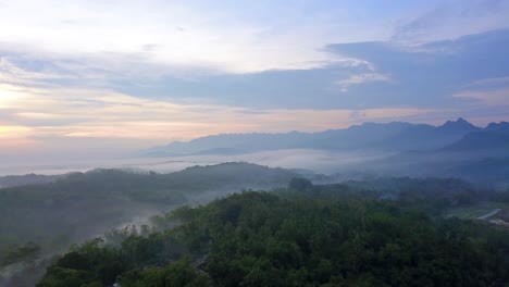 Tiro-De-Dron-Del-Bosque-Y-La-Colina-En-La-Mañana-Brumosa-Con-El-Cielo-Del-Amanecer-En-El-Fondo