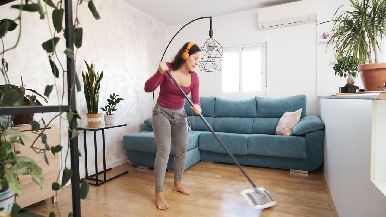 caucasian woman listening to music and singing with headphones while cleaning the floor at home