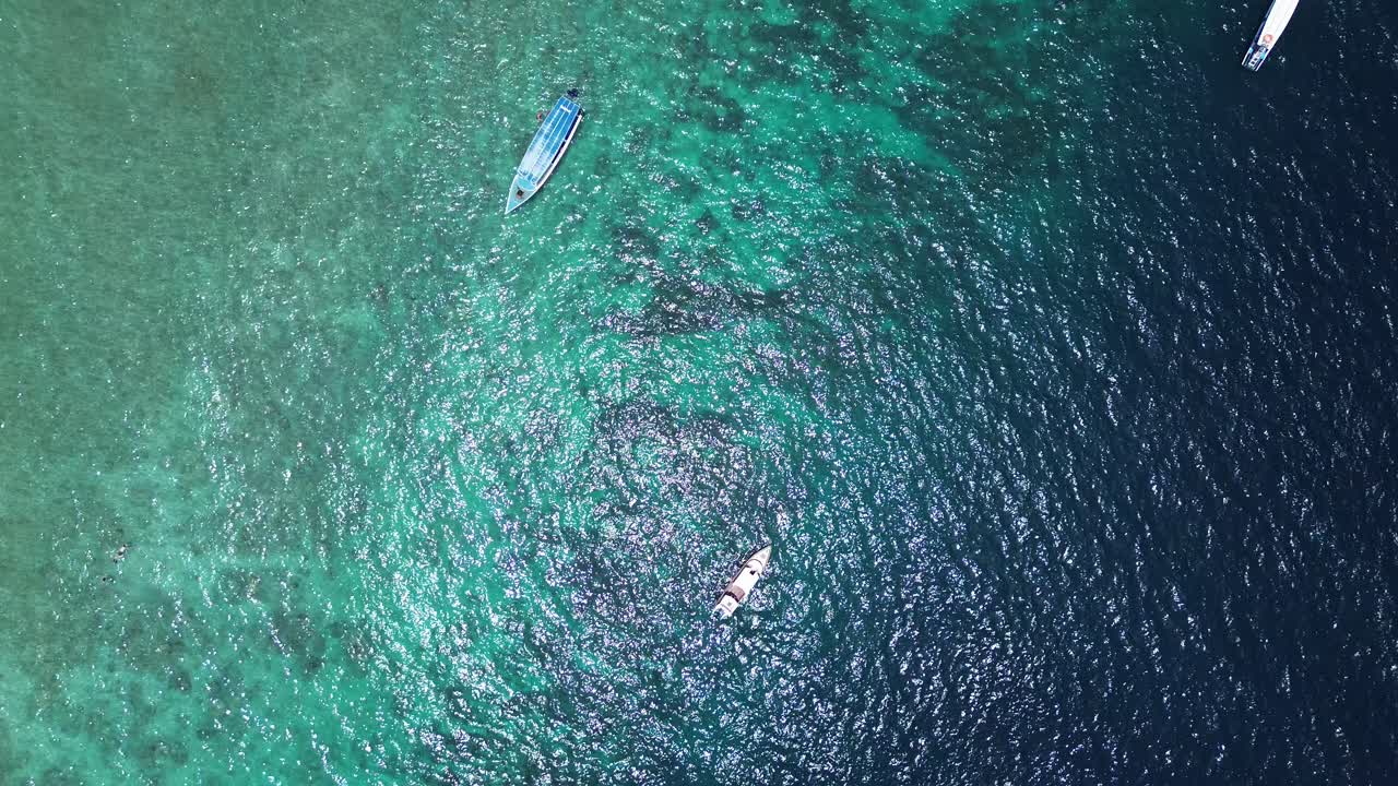 Zenithal zoom out of boats on vivid ocean surface with visible ripples and light reflection