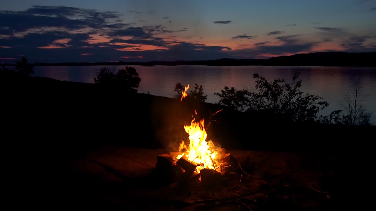 philip edward, island, ontario, canadá - una fogata está ardiendo junto al lago por la noche con el hermoso paisaje - toma amplia