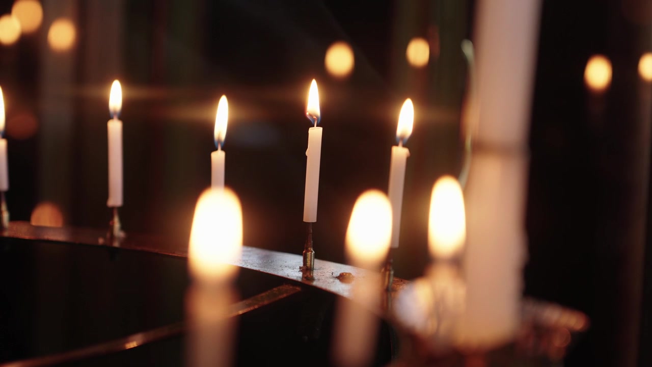 Diverse candele bianche accese su una rastrelliera metallica all'interno di un santuario buio con uno sfondo bokeh caldo