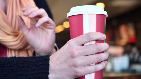 In-Einem-Café-Aufgenommener-Clip-Einer-Kaukasischen-Frau,-Die-Eine-Festliche-Kaffeetasse-Mit-Heißem-Kaffee-Oder-Tee-In-Der-Hand-Hält-Und-Mit-Ihren-Händen-Spricht