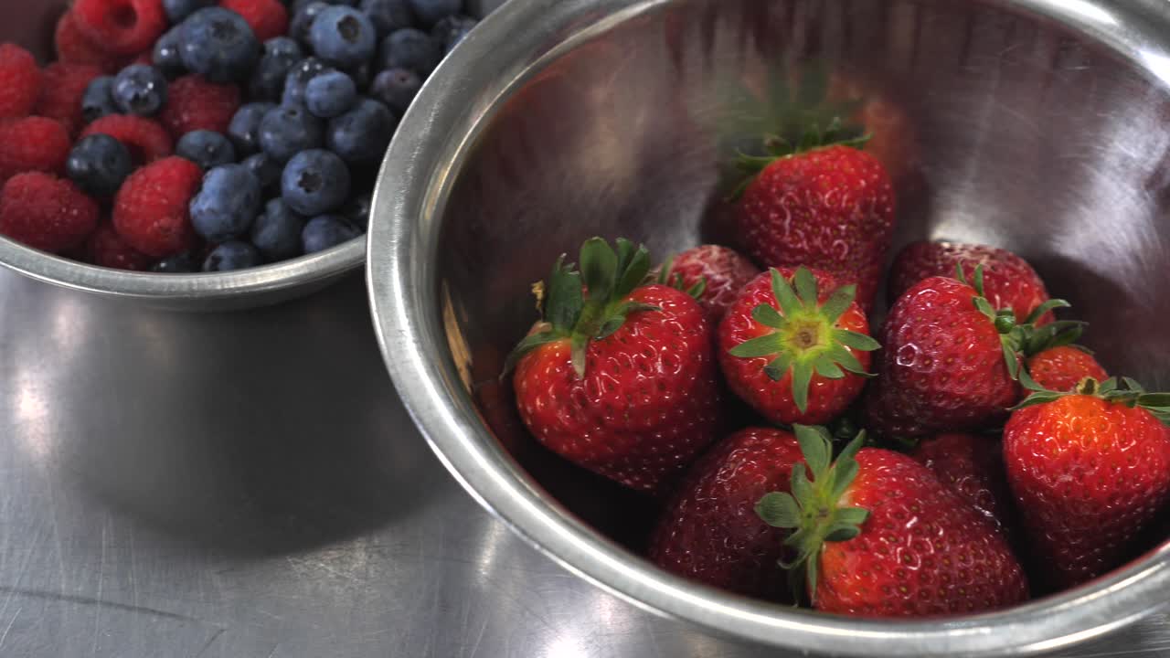벤치 위에 있는 상업용 주방에서 맛있는 과일 딸기, 블루베리, 라즈베리의 스테인리스 스틸 그릇 주위를 천천히 팬