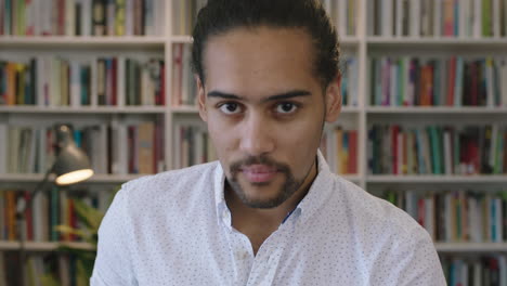 close up portrait of young hispanic man student enjoying texting browsing online using smartphone mobile app in library bookshelf background