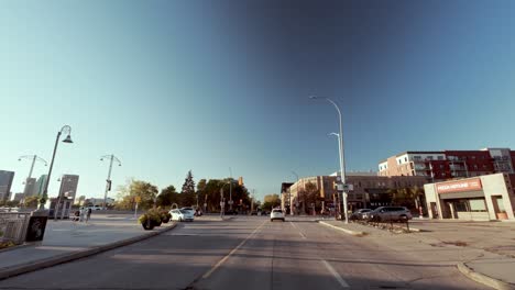 pov shot from car driving down empty street; river left, trees right; city skyline ahead; fall season