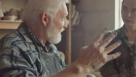 young woman learning pottery with senior artisan