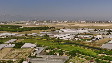 Antalya-Turquía-Aérea-V56-Tierras-De-Cultivo-Elevadas-En-Yenigöl-Llenas-De-Invernadero-De-Plástico-Con-Aislamiento-De-Aire-De-Horticultura-Con-Arroyo-Duden-Cruzando-Con-Vista-Al-Aeropuerto---Filmado-Con-Cine-Mavic-3---Julio-De-2022