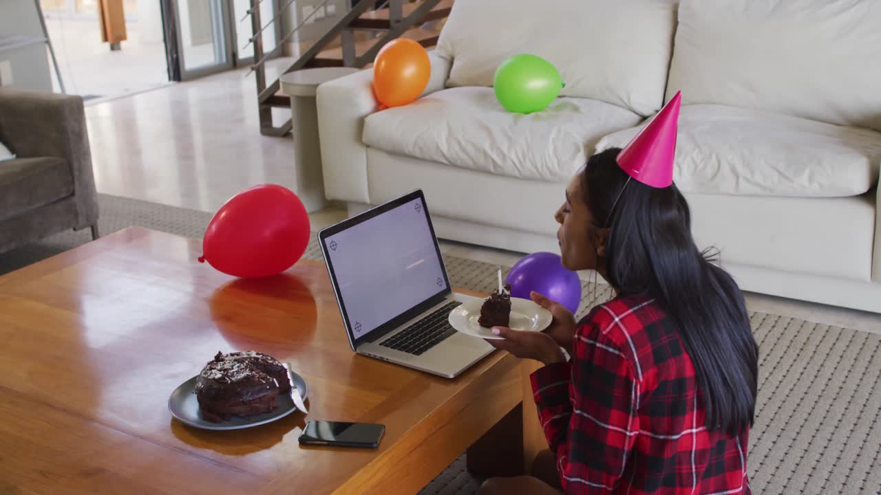 mujer de raza mixta usando una computadora portátil teniendo un video chat de cumpleaños sosteniendo un pastel