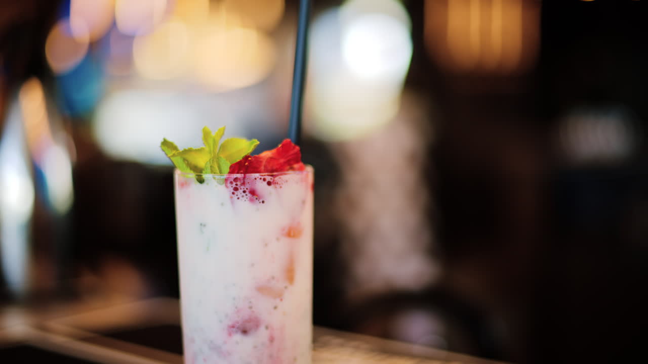 A strawberry drink with a black straw standing on a table at a restaurant