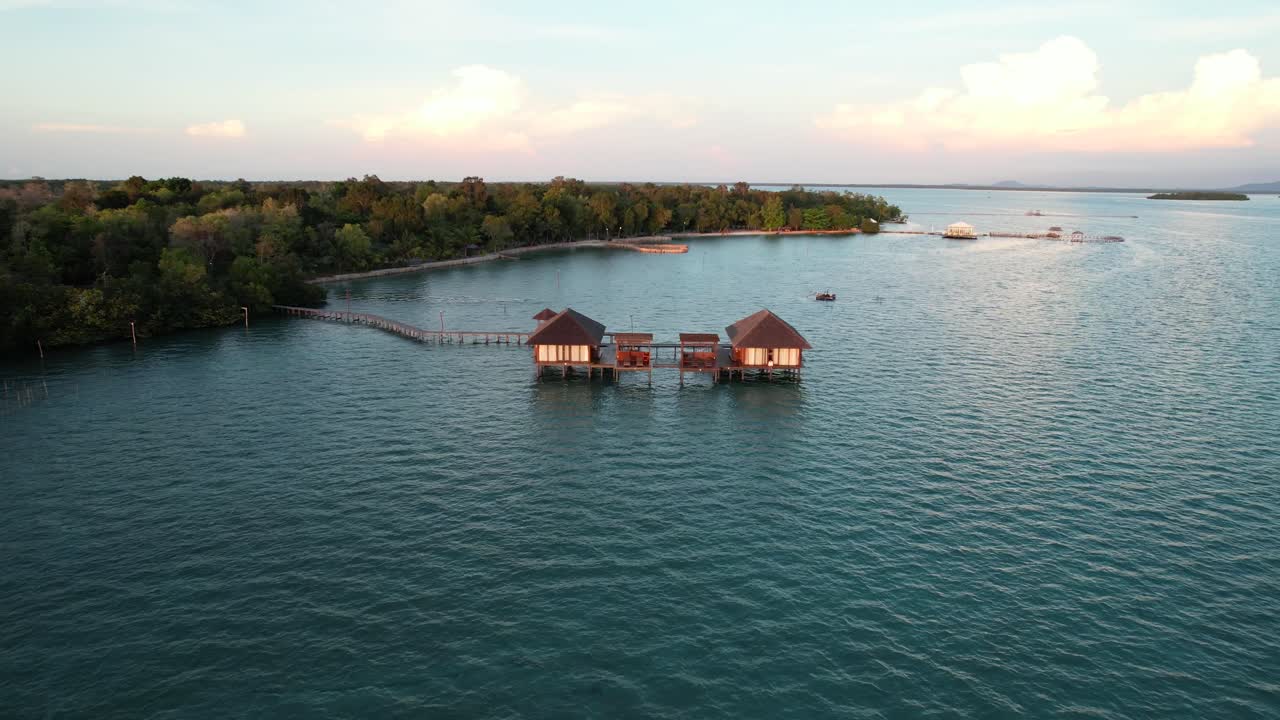 largo muelle de madera que conduce a dos bungalows sobre el agua resort al atardecer en la isla de leebong, belitung indonesia - paralaje aéreo