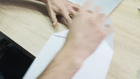 person folding a paper airplane at a desk