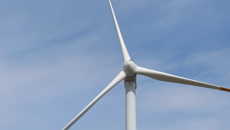 isolated single static wind turbine against blue sky and light clouds, drone crane shot