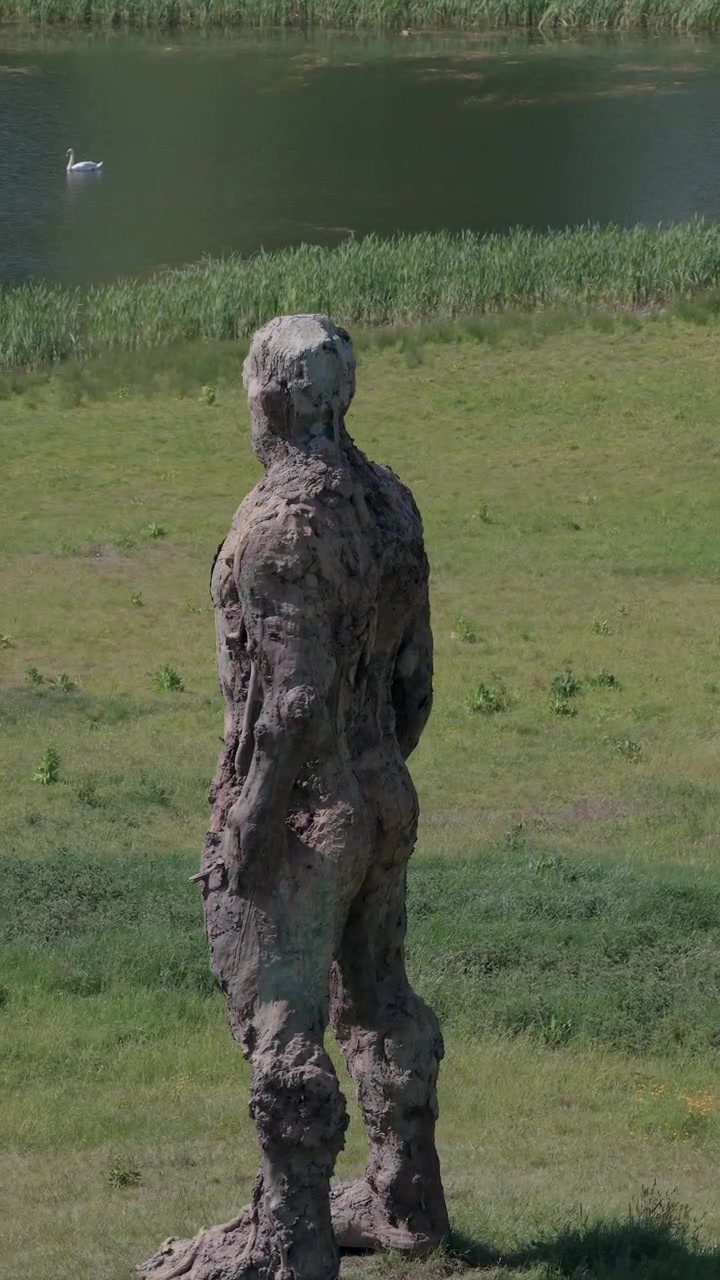 La statua di Yoxman si erge imponente, affacciandosi su un laghetto tranquillo e campi verdi lussureggianti nella campagna inglese, incarnando l'espressione artistica e la bellezza naturale.