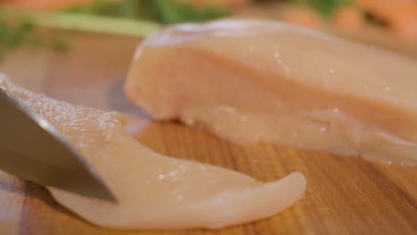 filete de pechuga de pollo rebanado con cuchillo en una tabla de cortar de madera