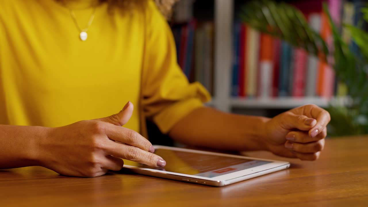 Close up woman scrolling on tablet at desk with bookshelf background