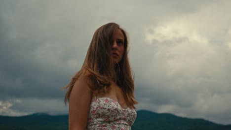 woman in a floral dress standing in front of a cloudy mountain range