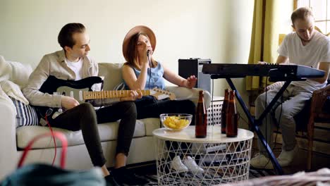 friends musicians are practising at home singing and playing guitar and keyboard. musical instruments, attractive creative people, friendship and hobby concept.