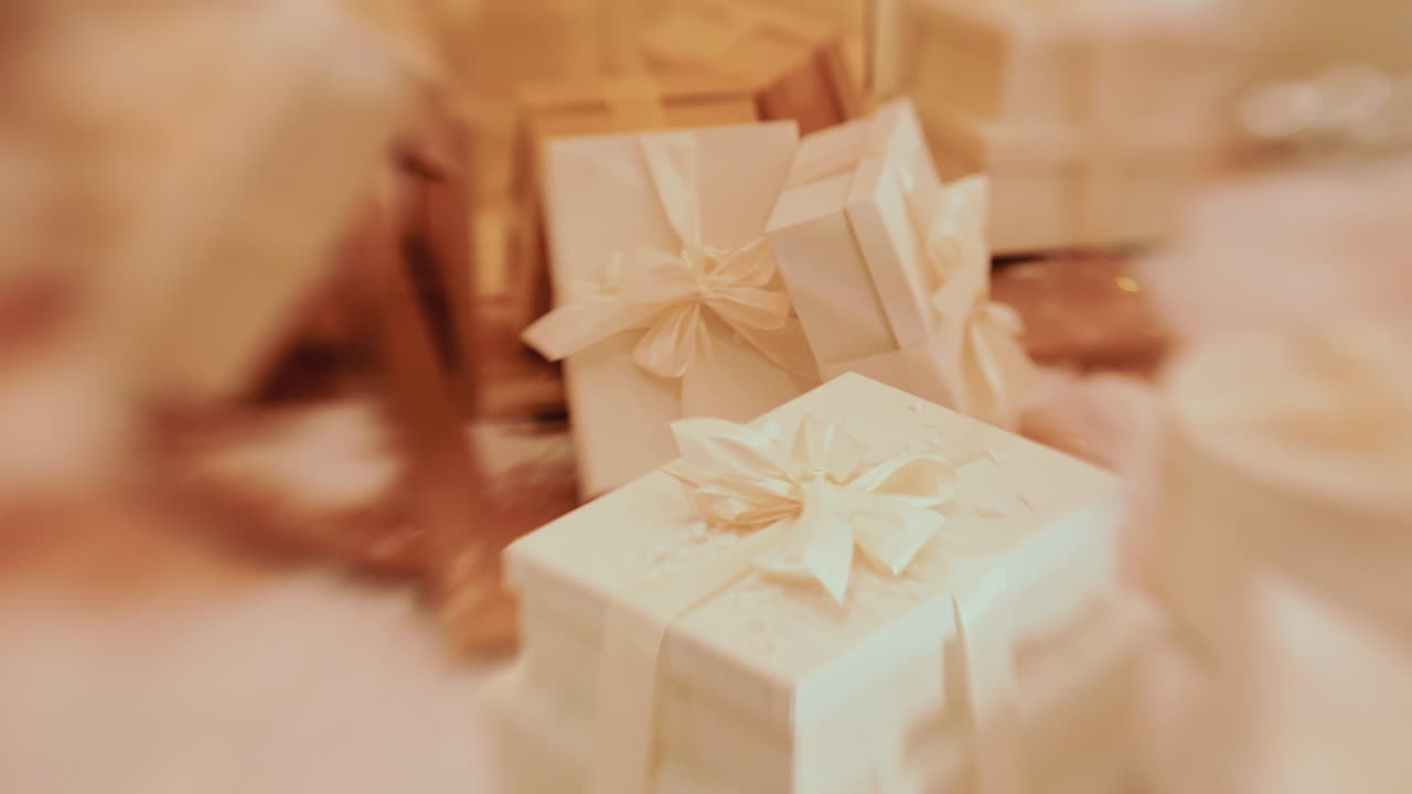 Palle di Natale dorate appese a una struttura, accanto a un pacco regalo bianco sospeso, con persone sfocate sullo sfondo
