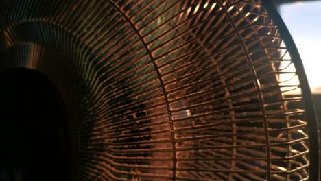 dusty indoor fan during sunset. low sun breaking through grid and propellers of ventilator causing lens flares. slow upwards camera movement revealing sun shining through window.