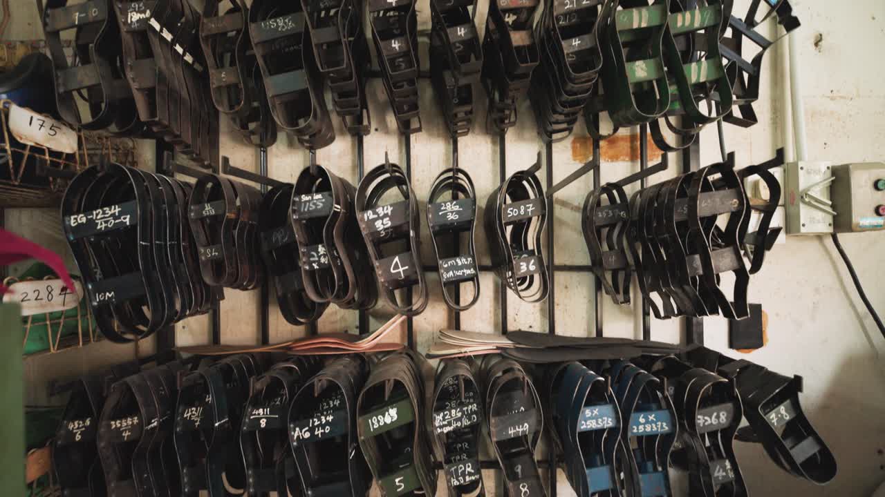 Gros plan de matrices et moules de découpe de semelles de chaussures suspendus dans un atelier, montrant des outils industriels, le processus artisanal et l'environnement de production de chaussures traditionnelles. UHD.