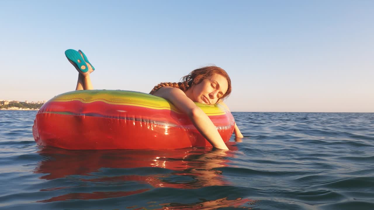 A woman swims in an inflatable bright life buoy swaying on the sea waves. Sea relaxation. Summer holidays.